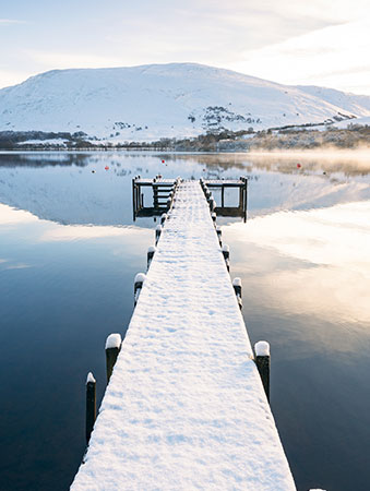 Snow covered jetty leading to a lake with snow covered mountains behind
